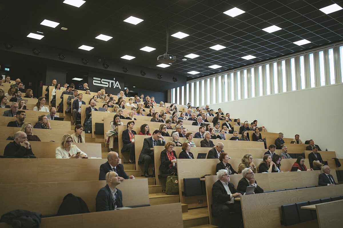 Blick in einen gefüllten Hörsaal mit Konferenzteilnehmer*innen