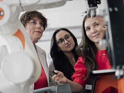 Professorin und Studierende beobachten einen Roboter-Arm bei der Arbeit