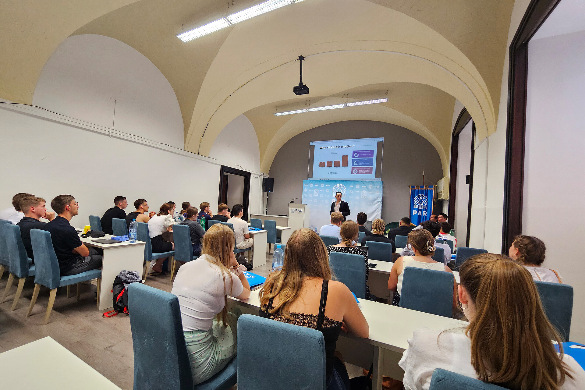 Studierende hören aufmerksam einem Dozenten im Hörsaal zu.