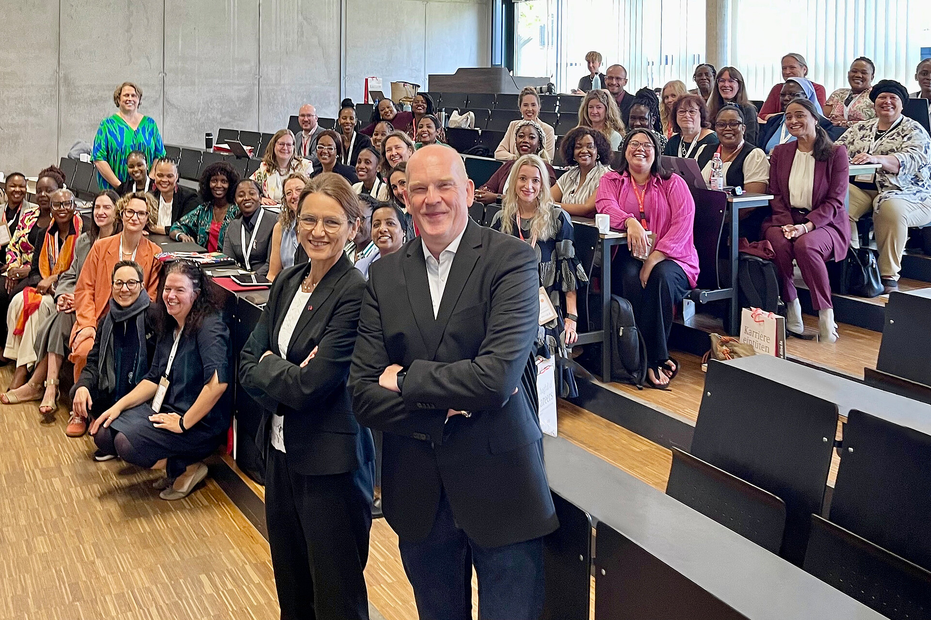 Gruppenfoto im Hörsaal der DHBW Mannheim während der FIREtalk Conference 2025. Zahlreiche internationale Teilnehmende sitzen und stehen lächelnd zusammen, zwei Konferenzleitende posieren vorne im Bild.