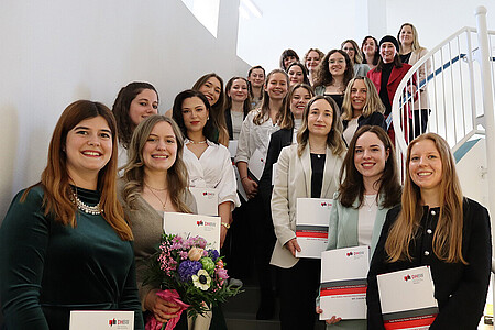Gruppenfoto der Absolventinnen mit Urkunden auf einer Treppe.
