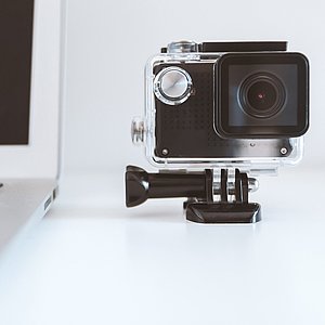 Foto einer Kamera mit einem Objektiv, die neben einem Laptop steht. 