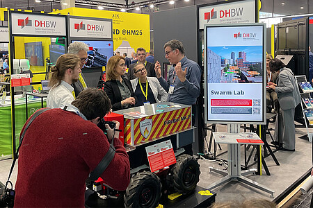 Mehrere Personen am Stand der DHBW, im Vordergrund ein Fotograf