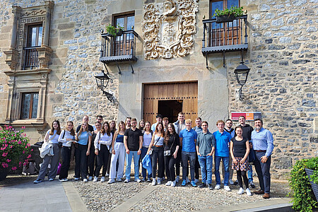 Gruppe von Studierenden steht für ein Gruppenfoto vor einem historischen Gebäude mit steinerner Fassade und Wappen in Mondragon.