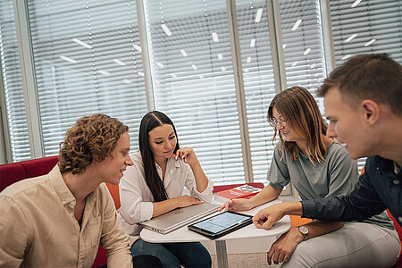 Vier junge Menschen sitzen an einem Tisch um ein Tablet herum.