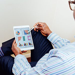 Foto einer Person, die ein Tablet und einen passenden Stift in der Hand hält. Auf dem Tablet sieht man verschiedene bunte Diagramme und Grafiken.