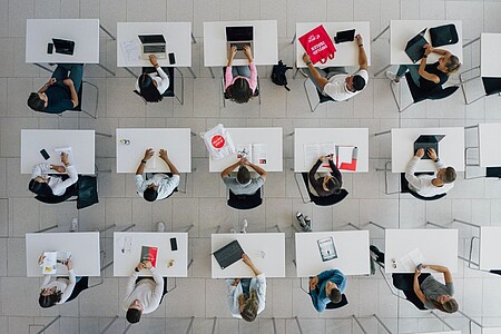 Studierende an einzelnen weißen Tischen aus der Vogelperspektive