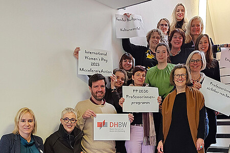 Die Gleichstellungsbeauftragten der DHBW auf einer Treppe mit Schildern mit der Aufschrift Gender Budgeting, Kulturwandel, International Women's Day 2025, Professorinnen sichtbar machen, PP2023 Professorinnenprogramm.