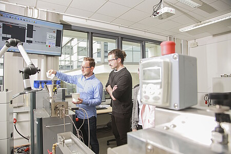 Personen arbeiten gemeinsam im Kunststofflabor mit einer Extrusionsanlage.