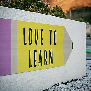 Foto eine Mauer, auf die ein gelber Bleistift gemalt ist. In dem Stift steht "Love to learn". 