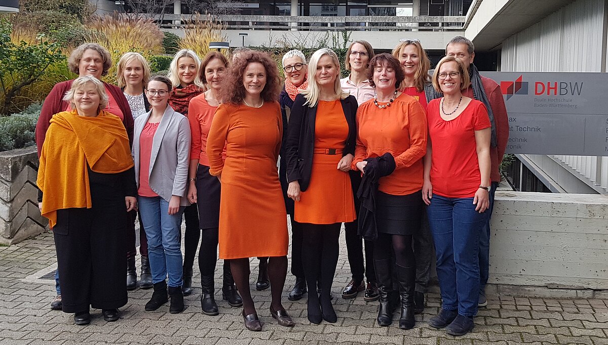 Gruppe aus Gleichstellungsbeauftragten und -referentinnen, alle tragen mindestens ein Kleidungsstück in Orange. 