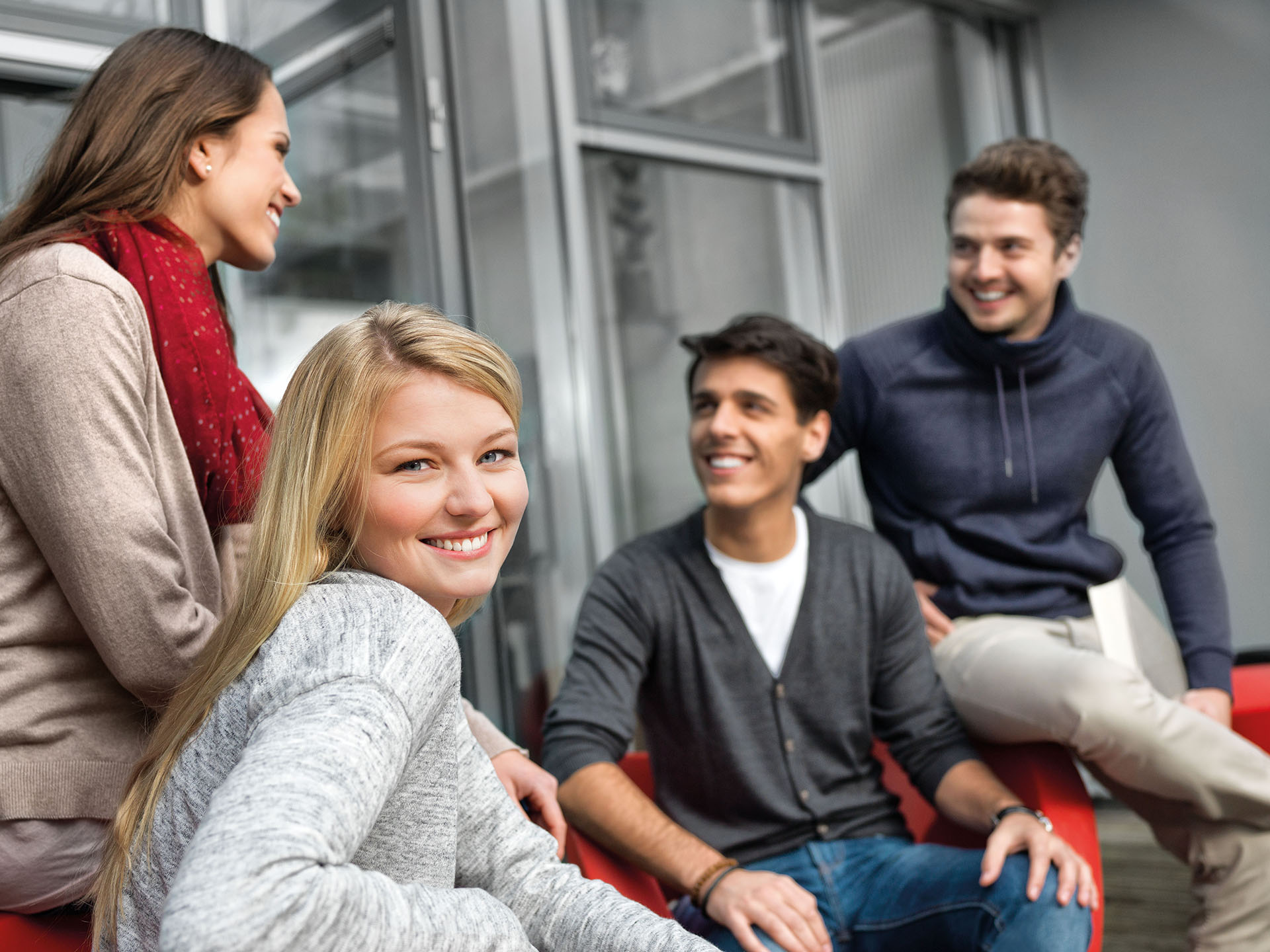 Zwei Studentinnen und zwei Studenten sitzen auf einem Sofa und unterhalten sich. Eine Studentin blickt nach vorne.