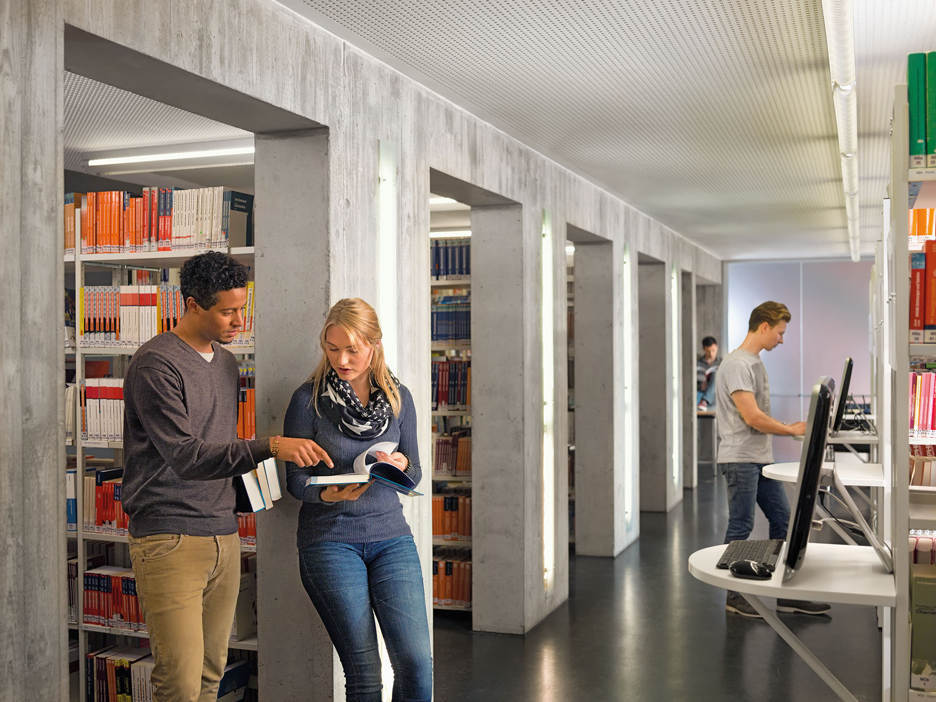 Ein Student und eine Studentin unterhalten sich über einen Text in einem Fachbuch in der Bibliothek an der DHBW Ravensburg Campus Friedrichshafen.