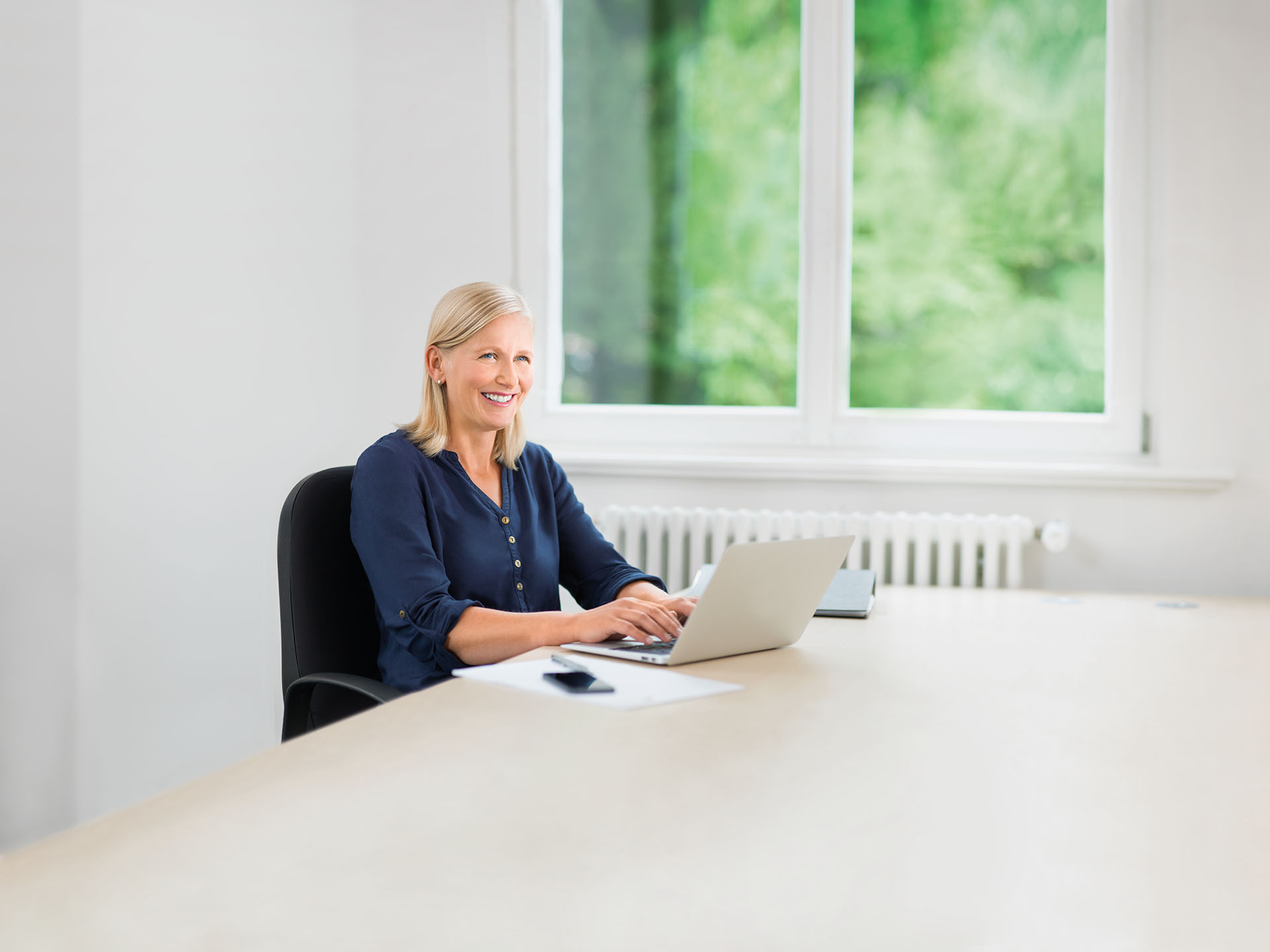 Ein Frau sitzt an ihrem Schreibtisch vor einem Laptop und tippt eine Bewerbung.