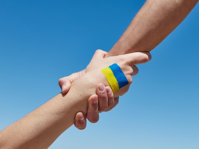 Foto zweier ineinandergreifender Hände, eine davon mit einer aufgemalten Ukraine-Flagge. 