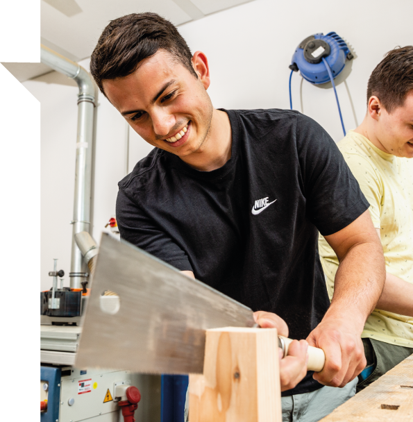 Ein Student bearbeitet in einer Werkstatt mit einem Hobel ein Stück Holz.