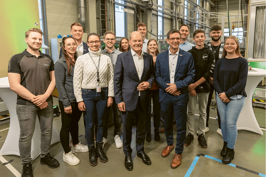 Gruppenfoto in Lagerhalle Bundeskanzler Scholz, Vizepräsident Stockburger, Studierende der DHBW und Mitarbeitende von Dualem Partner Hensoldt